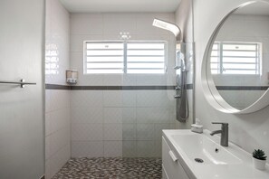 Une salle de bain moderne équipée d’une douche, d’un lavabo, d’un miroir et d’une fenêtre.
