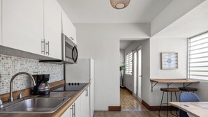 Cozinha moderna com pia de aço inoxidável, cafeteira e micro-ondas. Possui bancada de madeira e vista para uma sala de jantar com mesa e cadeiras.