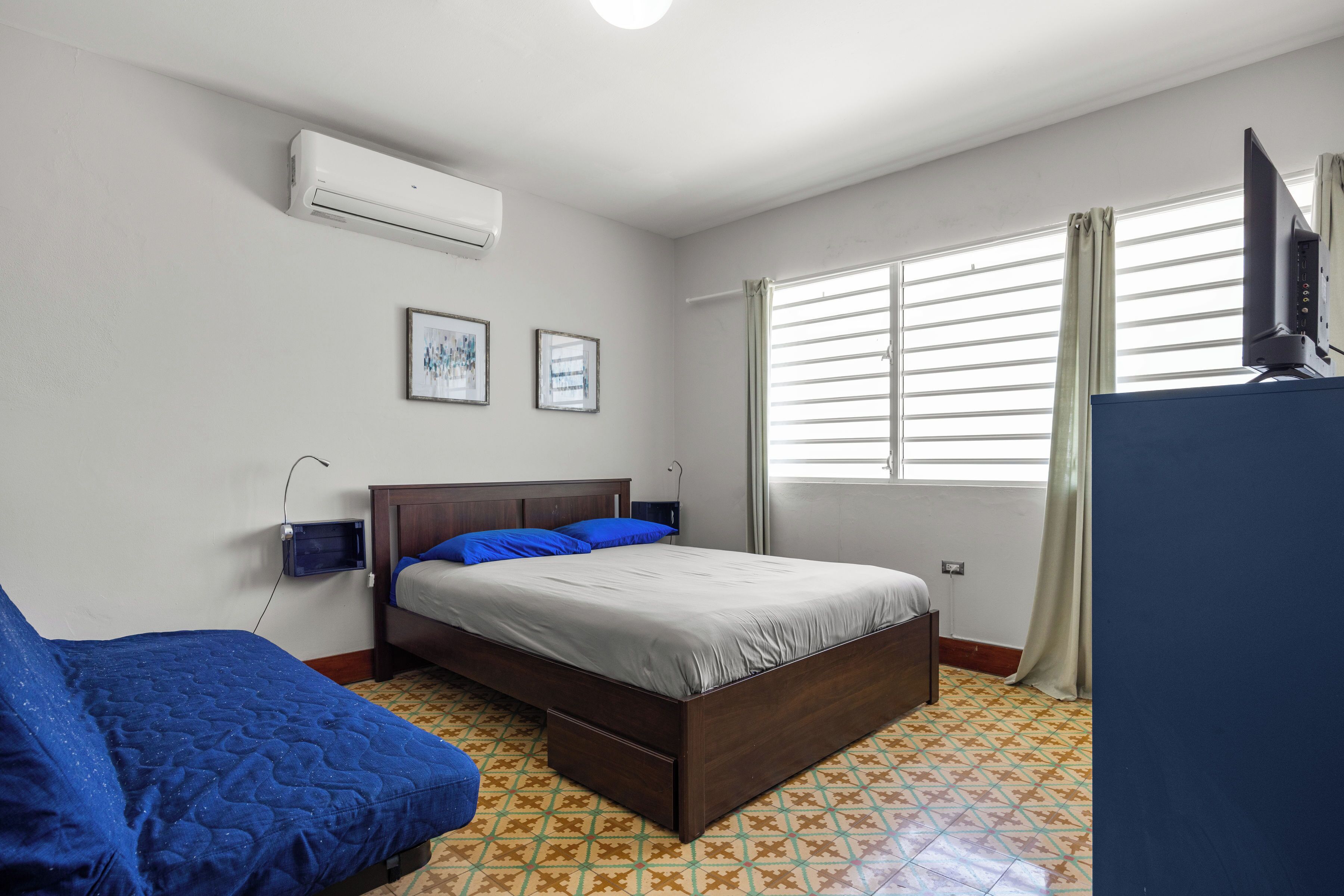 A bedroom with a bed, a blue couch, a TV, and a window with curtains.