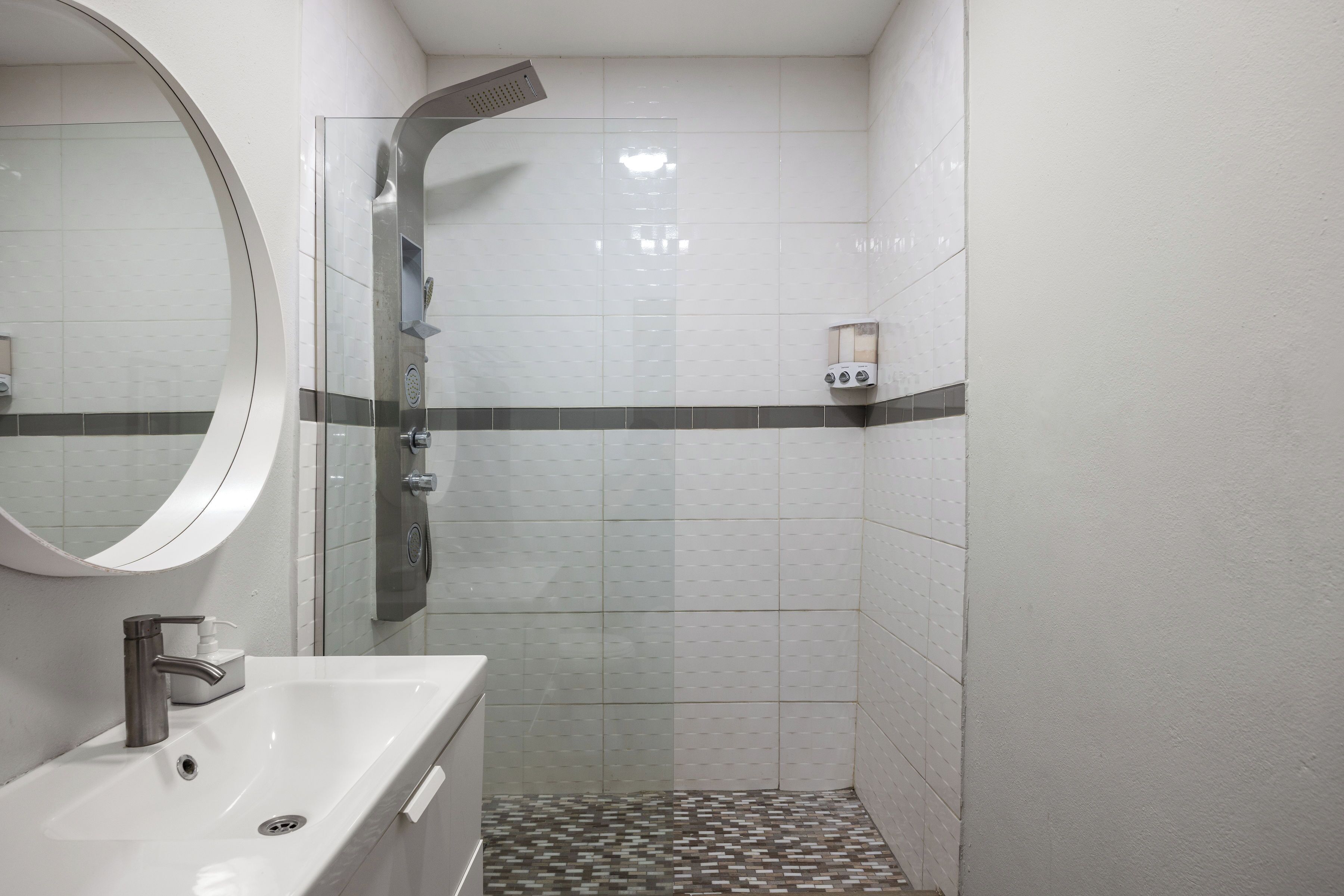 A bathroom with a sink, mirror, shower, and tiled walls.