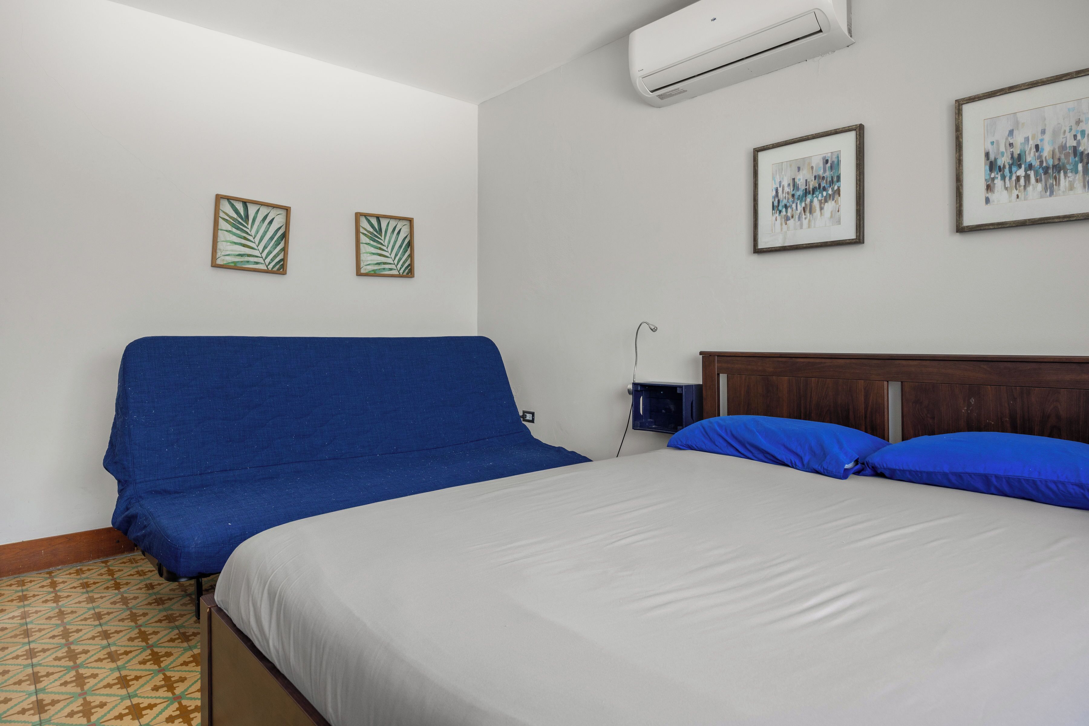 Una camera da letto con un letto, un divano blu e due opere d'arte appese al muro.