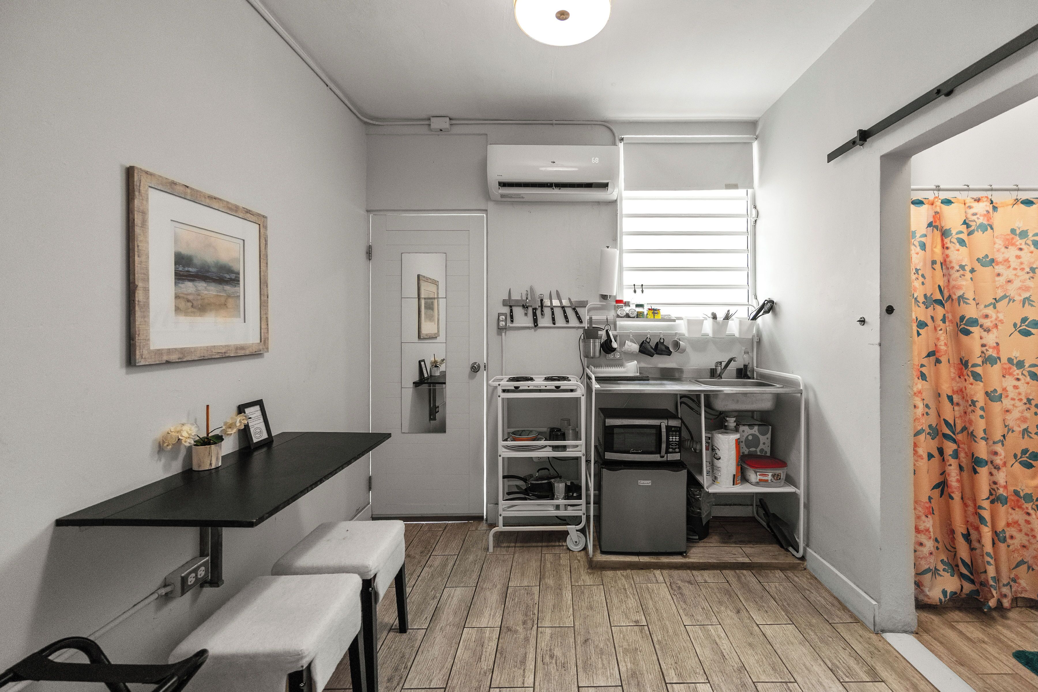 A compact kitchen with a dining area, a microwave, a small refrigerator, and a white air conditioning unit.