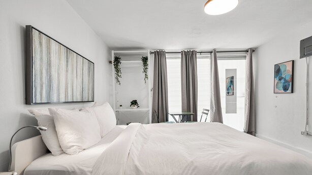 Quarto moderno com uma cama grande, mesa de cabeceira, planta pendente, escrivaninha e uma cadeira.