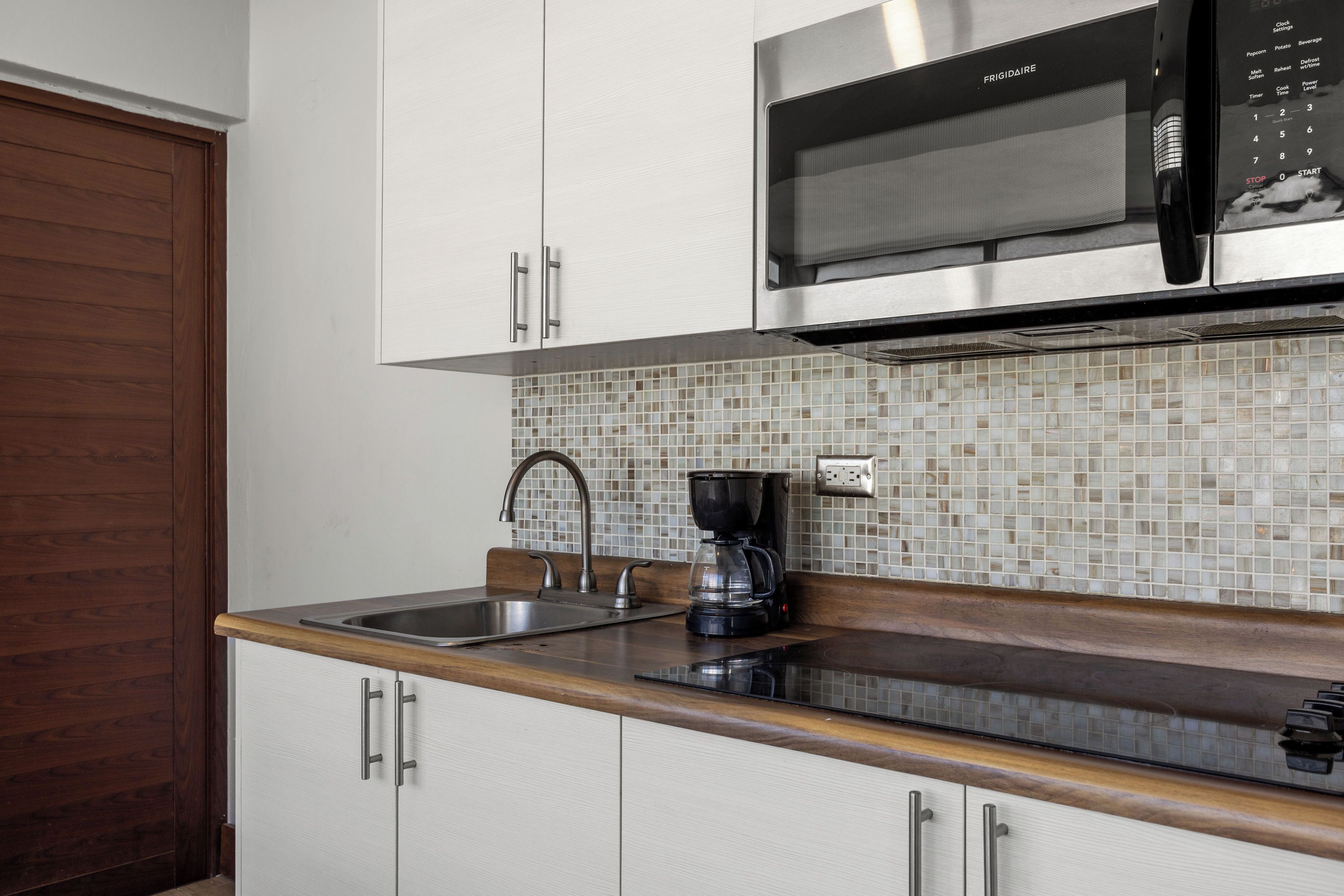 A kitchen with white cabinets, a stainless steel microwave, a coffee maker, and a tiled backsplash.