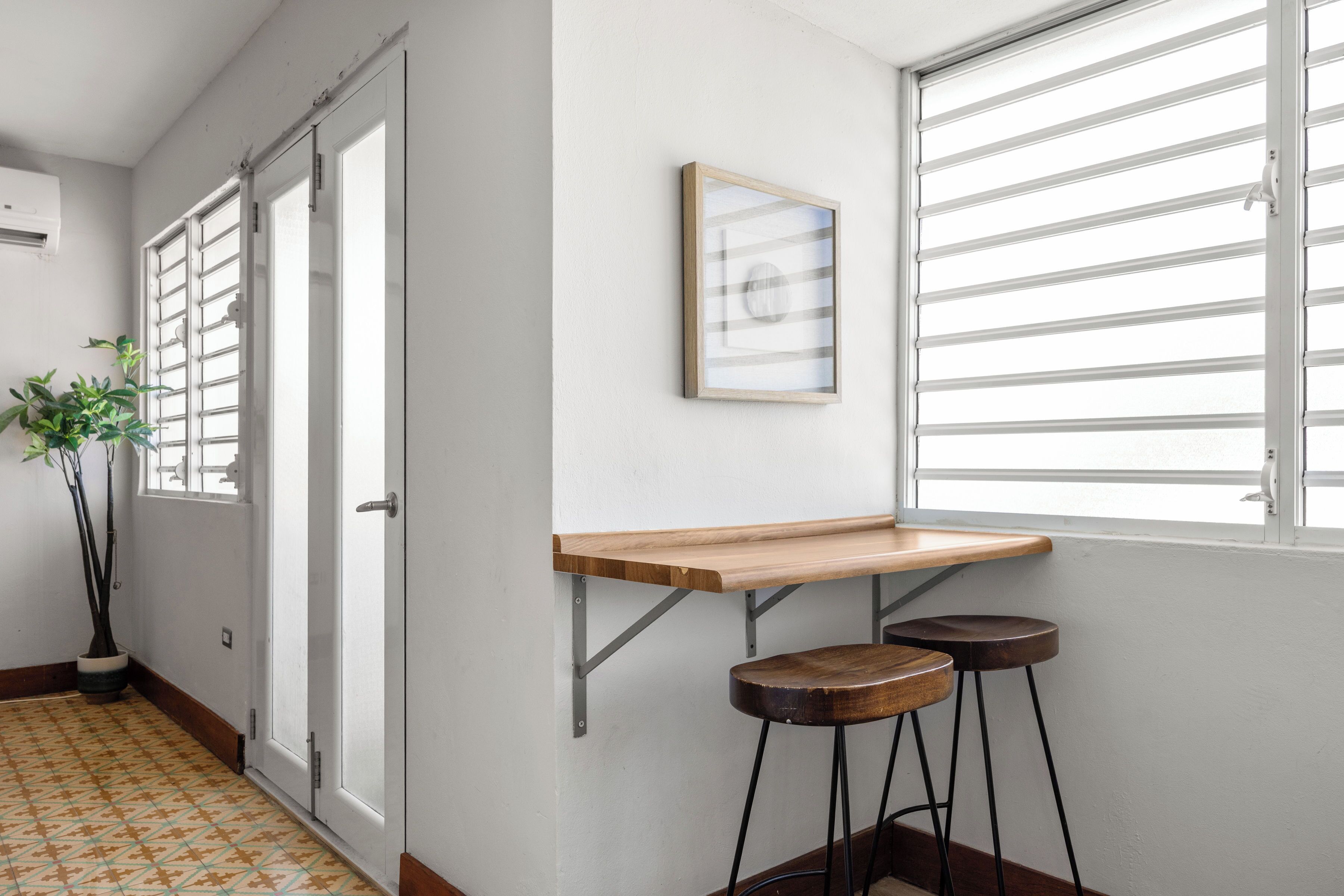 Un couloir avec un banc en bois, deux tabourets, une plante en pot et un tableau encadré accroché au mur.