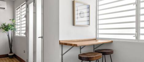 Un couloir avec un banc en bois, deux tabourets, une plante en pot et un tableau encadré accroché au mur.