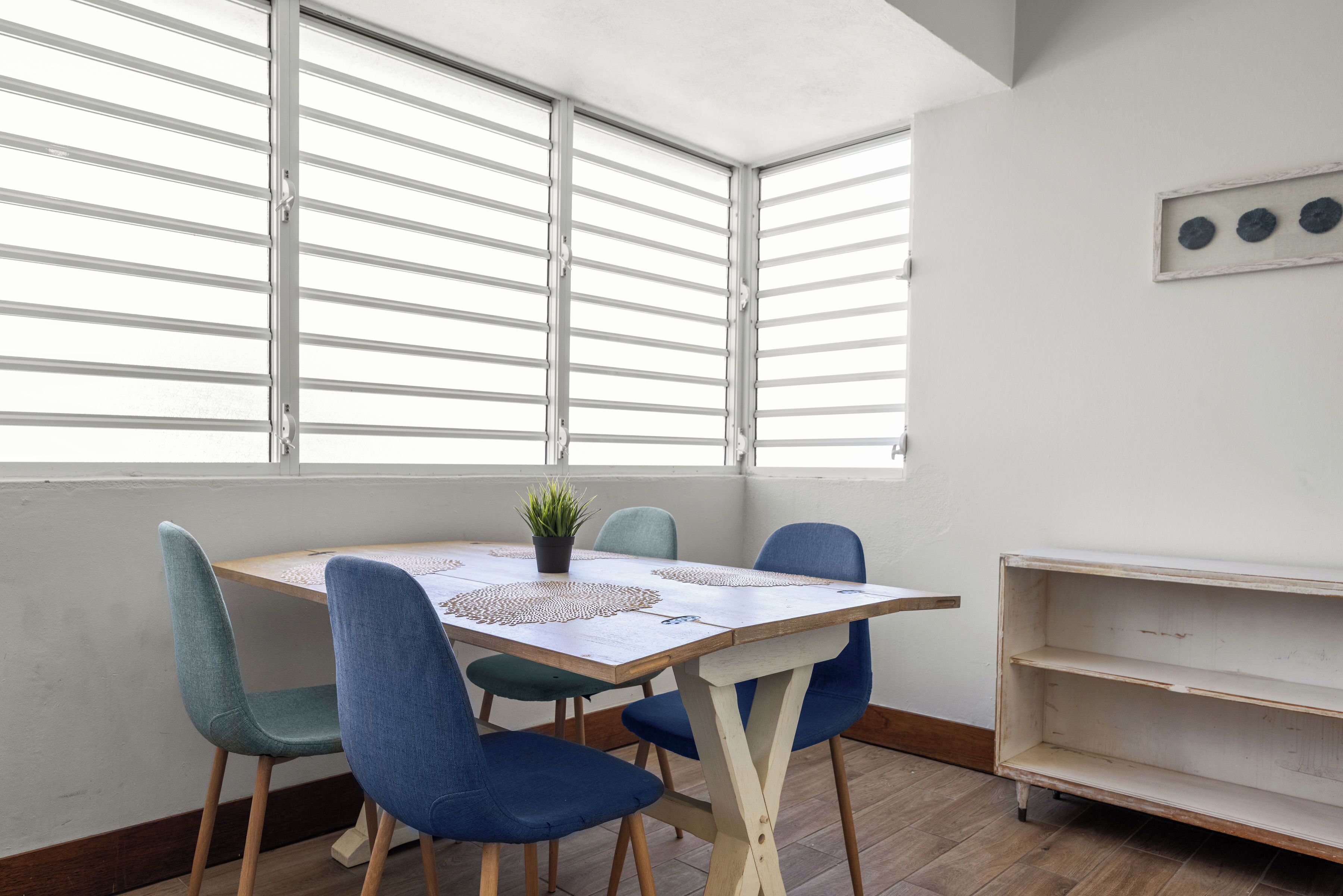 A room with a wooden table, blue chairs, a small potted plant, and a white shelf.