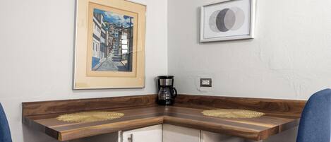 Ein Schreibtisch an der Ecke mit zwei Stühlen, einer Kaffeemaschine und zwei gerahmten Bildern an der Wand.
