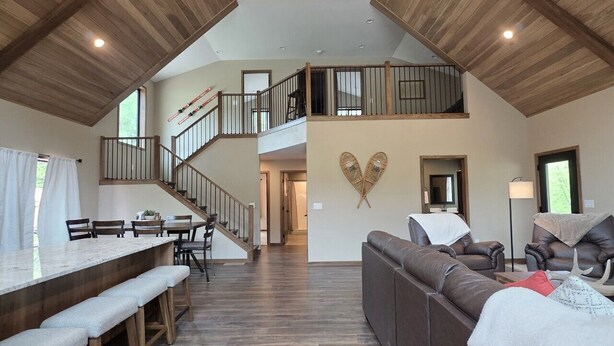 A spacious loft with a high ceiling, wooden beams, a dining area with benches, a sofa, and a staircase leading to an upper level. - Deadwood Cabin-Sleeps 12-Hot Tub-4X4 Trails-Central (Deadwood)