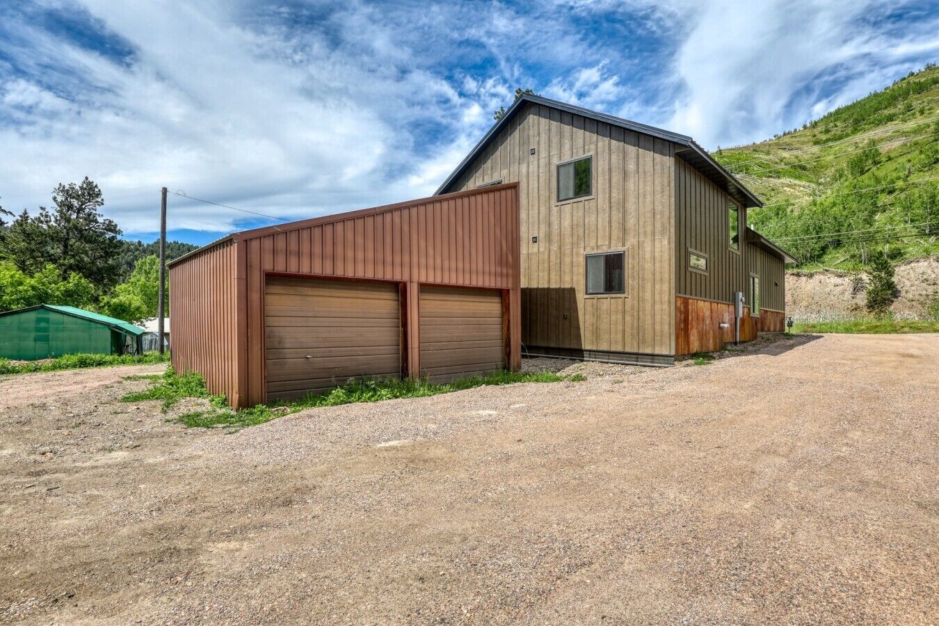 A two-story building with a gravel driveway and a green-roofed structure in the background.