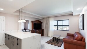 A modern living room with a marble island, a brown leather sofa, a TV, and a large window with a city view. - Cozy 2-bedroom condo in adorable Orlando with AC and gym access (Orlando)