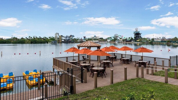 A lakeside patio with tables and chairs, a boat dock, and a distant amusement park. - Cozy 2-bedroom condo in adorable Orlando with AC and gym access (Orlando)