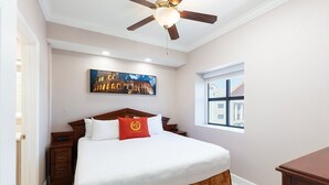 A bedroom with a bed, a ceiling fan, a nightstand, a bedside table, a window, and a painting of the Colosseum. - Cozy 2-bedroom condo in adorable Orlando with AC and gym access (Orlando)