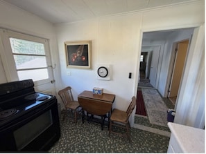 Une cuisine équipée d’une cuisinière, une table à manger avec des chaises, une horloge et un tableau encadré accroché au mur.