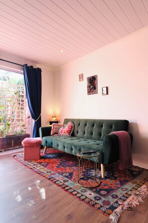 A room with a green sofa, a patterned rug, a small round table, and a window with curtains. - Flamingo Palm House - boutique-inspired stay (Cape Town)