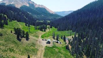 A mountainous landscape with a dirt path, a small cabin, and dense forest.