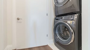 Une buanderie équipée d’un lave-linge et d’un sèche-linge superposés, d’une porte blanche et d’un plancher en bois.