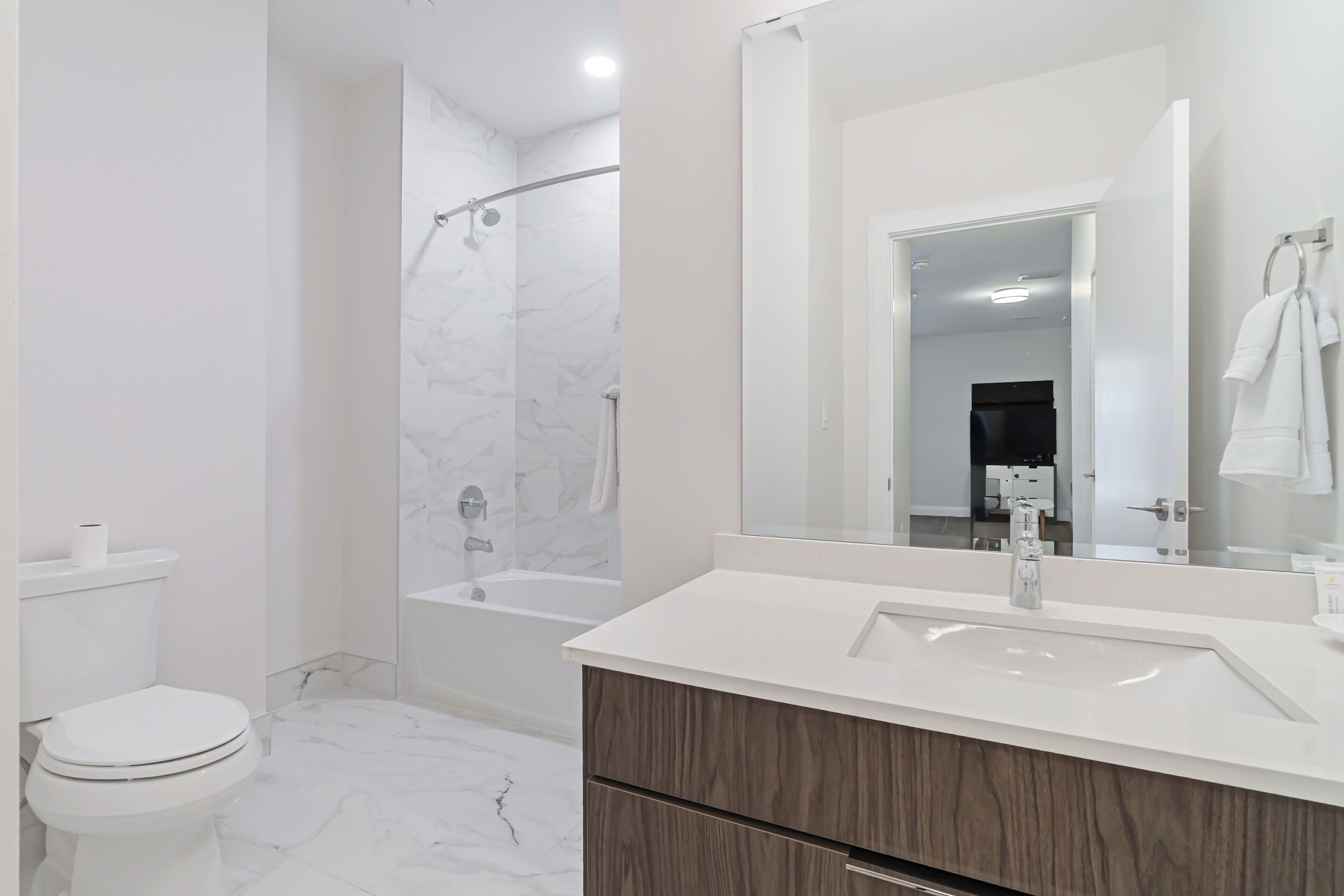 A modern bathroom with a toilet, a shower, a sink, and a mirror.