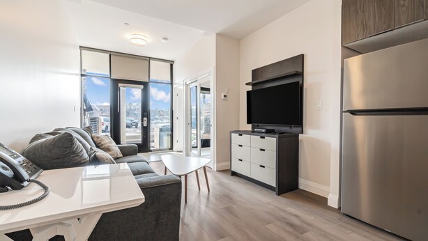 Un appartement moderne comprenant une cuisine, un coin repas, un salon avec un canapé et une grande fenêtre donnant sur la ville.