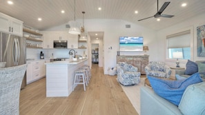 Une cuisine spacieuse avec des meubles blancs, un îlot central et un coin repas agrémenté de chaises à motifs.