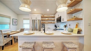 Une cuisine moderne dotée d’un îlot central, d’appareils électroménagers en acier inoxydable et d’un coin repas avec des chaises en osier.