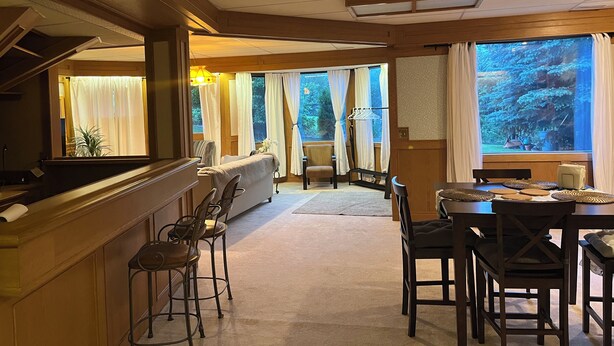 Et hotelværelse med spiseplads, bar og store vinduer med gardiner.