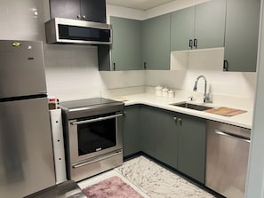 Una cocina compacta con refrigerador, horno, microondas, lavamanos y armarios.