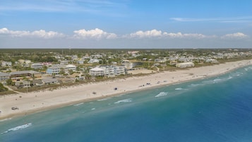 Vista aérea de un pueblo costero con propiedades frente a la playa, una playa de arena y un océano azul cristalino.