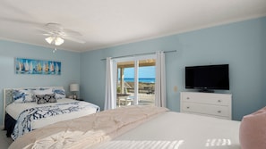 A bedroom with a bed, a TV, a ceiling fan, and a painting of sailboats. - Pink Flamingo by the Sea Avantstay Walk to Beach + Ocean Views + Outdoor Dining Near Pier Park + Panama City Beach (Panama City Beach)