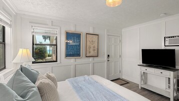 Habitación de hotel con cama, televisión, lámpara y mapas náuticos enmarcados en la pared.