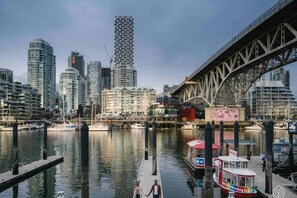 Un paysage urbain au bord de l’eau, avec des immeubles modernes de grande hauteur, un pont et un quai pour bateaux.