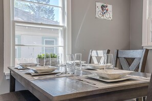 A dining table set with clear glassware, plates, and cutlery, positioned near a window with a view of a building. - NEW! Starlight Stay | Outdoor Oasis w/ Game Room! (Fruita)