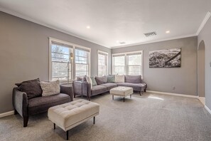 A spacious living room with a gray carpet, a gray sofa set, a beige ottoman, and a painting on the wall. - NEW! Starlight Stay | Outdoor Oasis w/ Game Room! (Fruita)