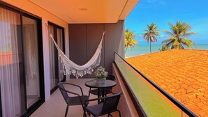 Ein Balkon mit Tisch und Stühlen, einer Hängematte und Blick auf den Strand und Palmen.