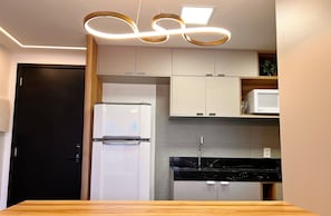 A modern kitchen with a refrigerator, microwave, and black countertop. - Altamare - Miramar Hospedagens  (João Pessoa)