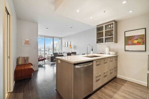 A modern kitchen with a central island, a dining area with a view, and a living space with a sofa and a coffee table. - Modern 1-Bed Condo | Mountain Views | 10 mins > DT (Vancouver)