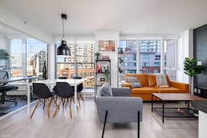 A modern living room with a dining area, large windows, and a city view. - Downtown Luxurious 2BD|Pool |Parking|Hot Tub|Sauna (Vancouver)