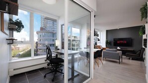 A modern apartment with a dining area, a living room with a TV, and a large window overlooking a cityscape. - Downtown Luxurious 2BD|Pool |Parking|Hot Tub|Sauna (Vancouver)