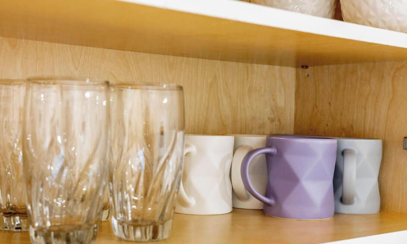 Una repisa con vasos de vidrio transparente y tazas de cerámica.