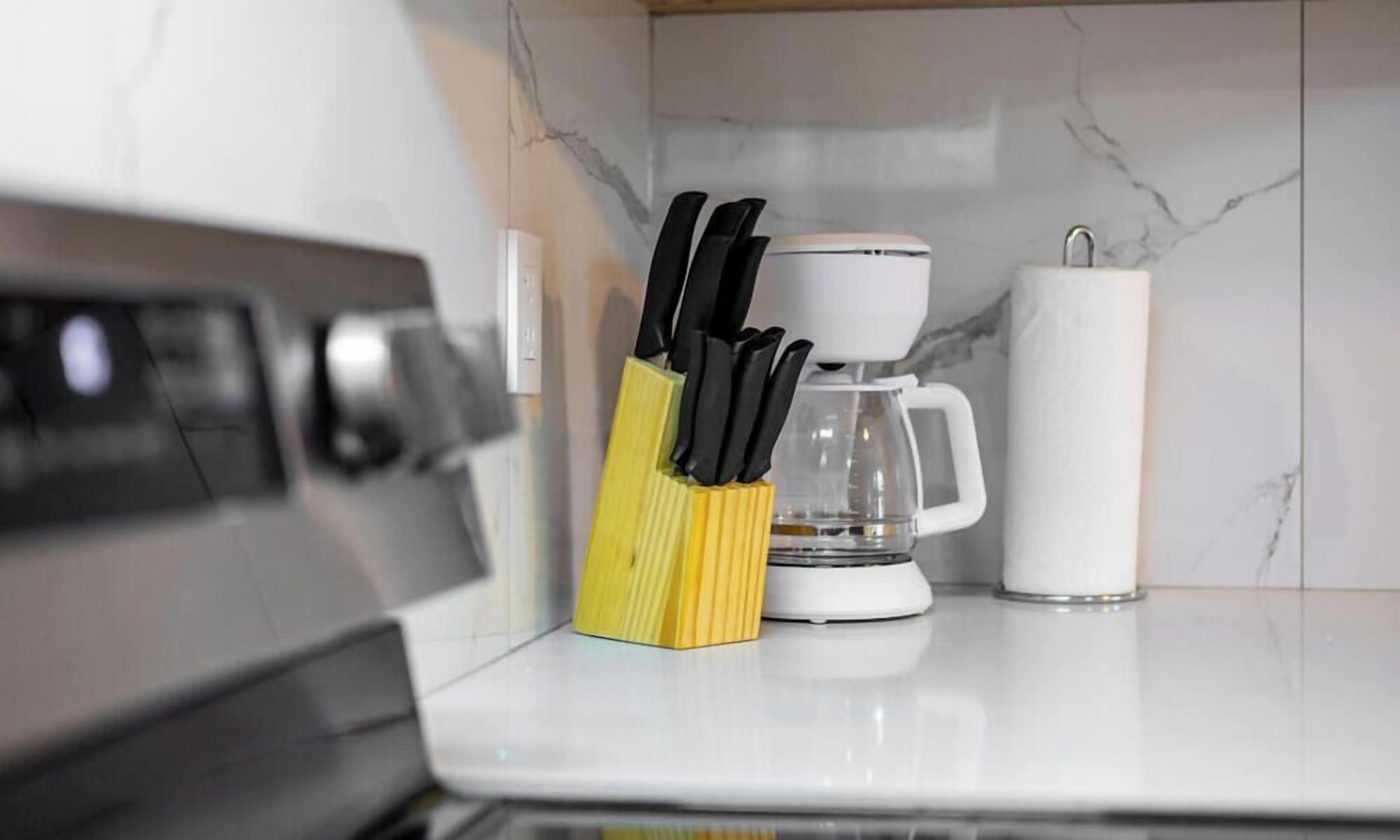 Een keuken met een koffiezetapparaat, een witte mok en een messenblok op het aanrecht.