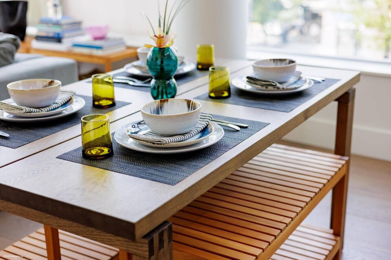 Una mesa con platos, tazones y vasos, colocada sobre un banco de madera.