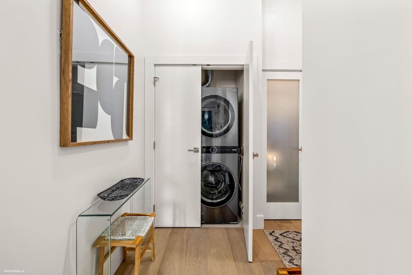 Una sala de lavandería con dos lavadoras, un banco de vidrio y una puerta con paneles de vidrio esmerilado.