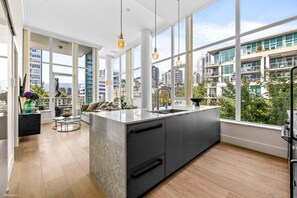 A modern kitchen with large windows, a central island, and a view of high-rise buildings. - Luxury Waterfront 2BR| Harbor View| Pool| Hot Tub (North Vancouver)