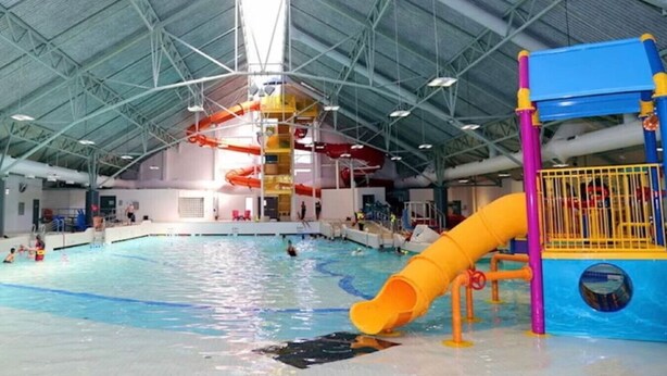 An indoor swimming pool with a yellow slide, a water play area, and a high ceiling with visible structural beams. - Modern 2BR Retreat |Free Parking |Desk| Fast Wi-Fi (Surrey)