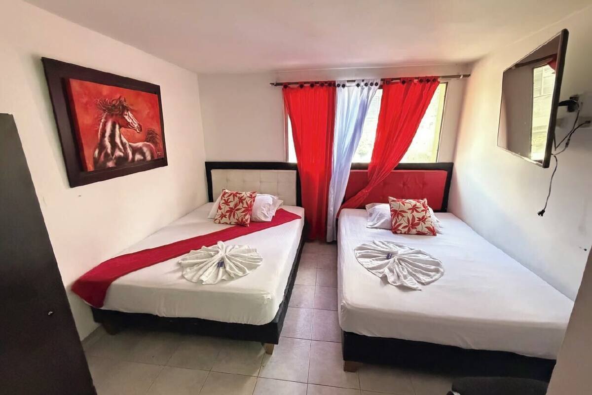 A room with two beds, a red curtain, a painting, and a TV on the wall.