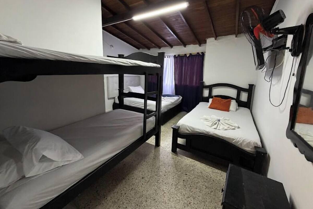 A dormitory room with bunk beds, a ceiling fan, and a window with curtains.