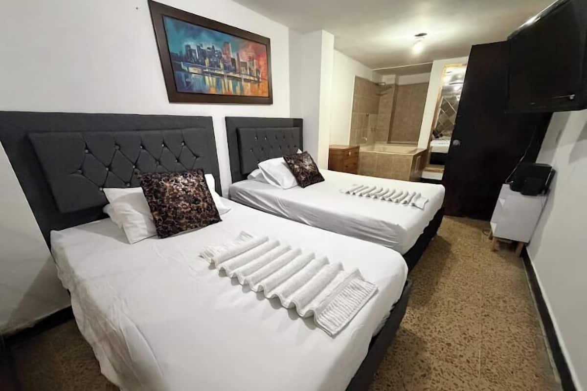 Two beds with white linens, a cityscape painting on the wall, and a shower area in the background.