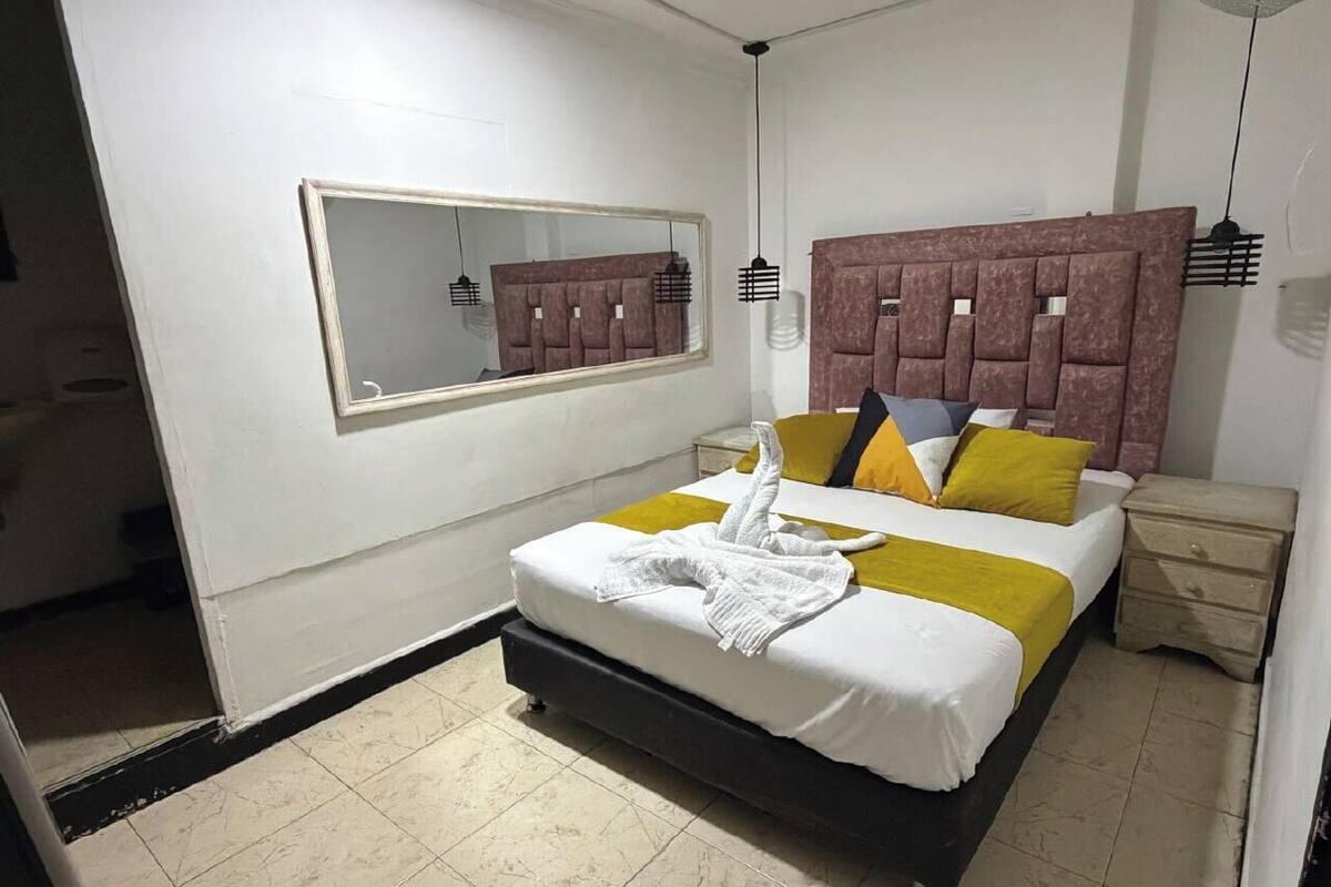 A bedroom with a bed, a nightstand, a mirror, and a headboard.