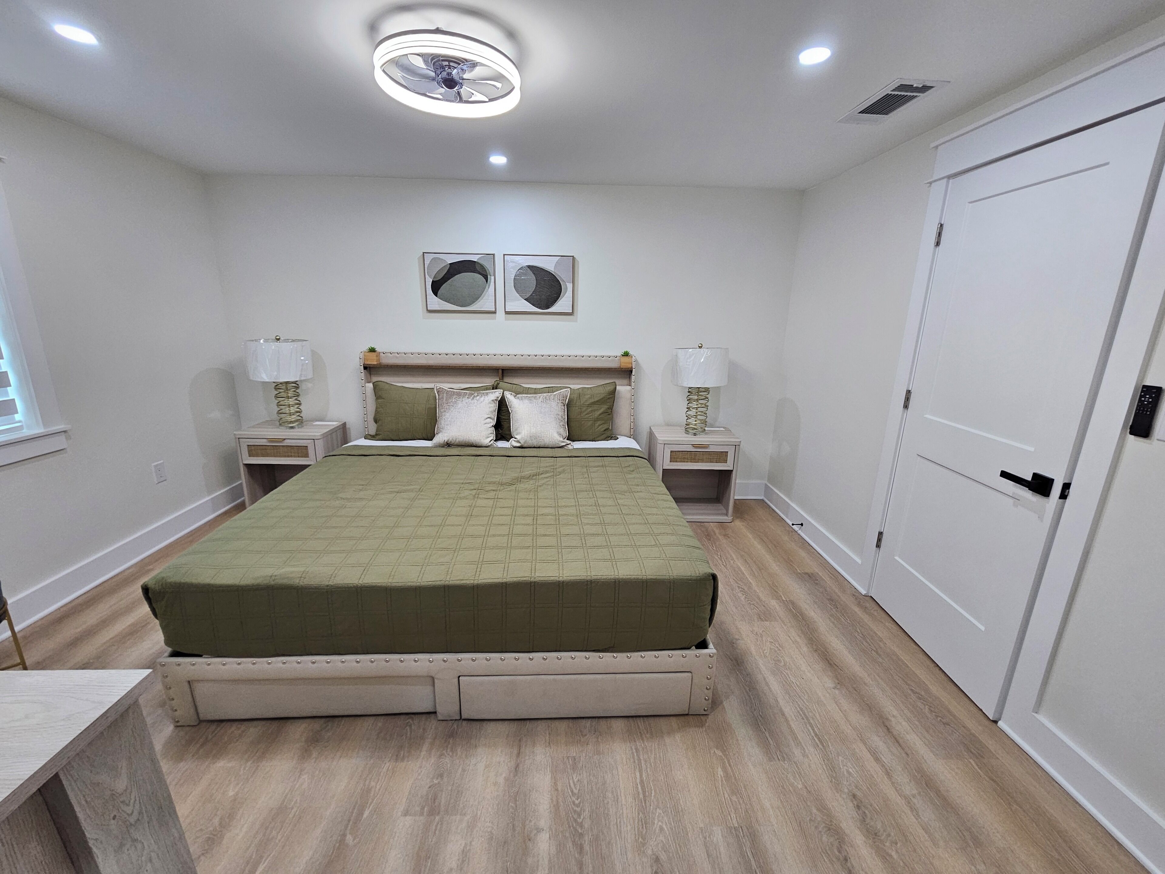 A bedroom with a bed, bedside tables, a ceiling fan, and a door.