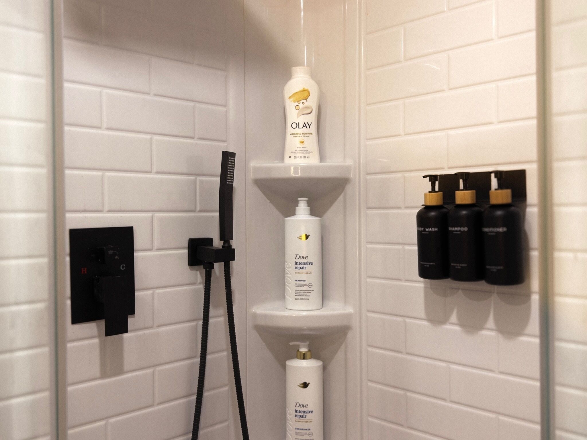 Ein Duschbereich mit weiß gefliesten Wänden, einer Handbrause und Regalen mit Dove Intensive Repair Shampoo, Conditioner und Duschgel.